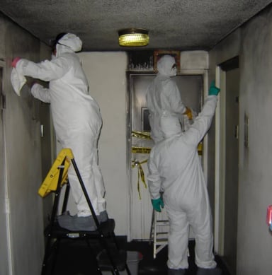 Workers in protective gear clean a damaged hallway.